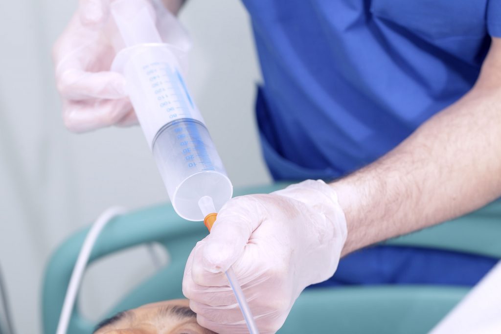 A nurse is holding a syringe and putting it in the mouth of a patient.